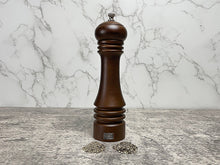 Afbeelding in Gallery-weergave laden, Een sfeerbeeld van een chocolade bruine beukenhouten pepermolen met een hoopje fijne en groffen peper.